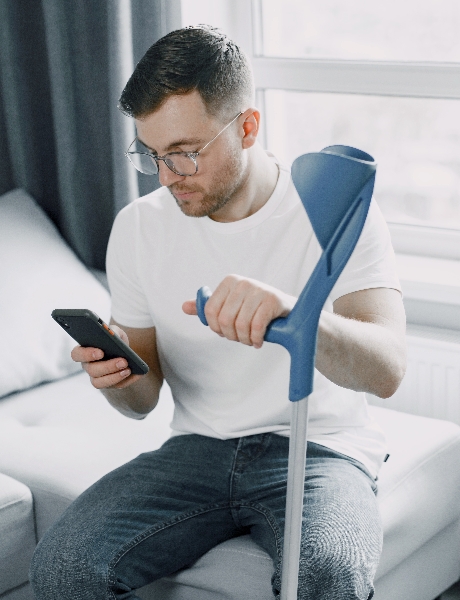 Junger Mann mit Gipsbein nutzt zu Hause sein Smartphone